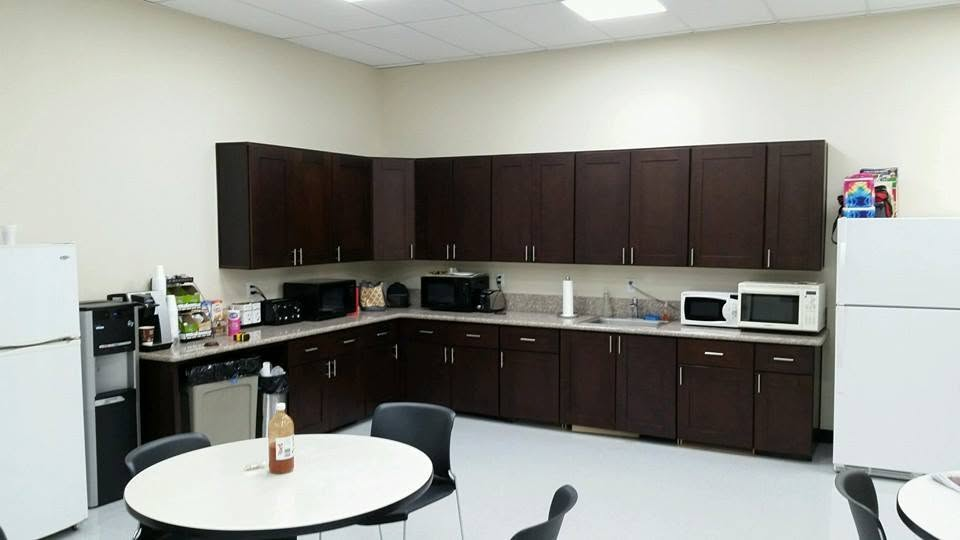 Modern office break room with dark wood cabinetry, white appliances, and round dining tables