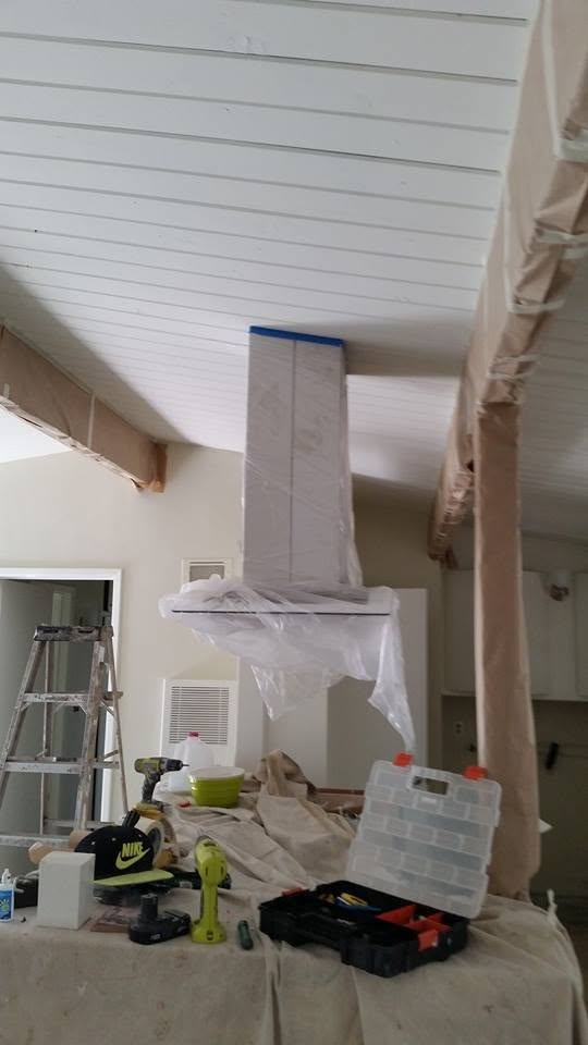 Kitchen range hood wrapped in protective plastic during renovation, surrounded by tools and materials