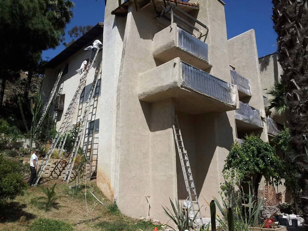 Workers on ladders performing exterior renovation on multi-story residential building