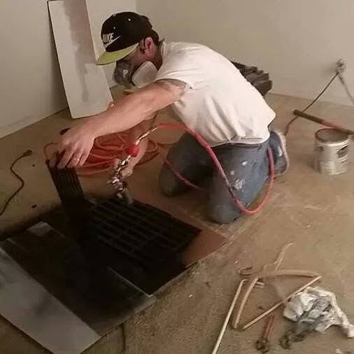Worker in white shirt and cap applying red material to floor opening during renovation