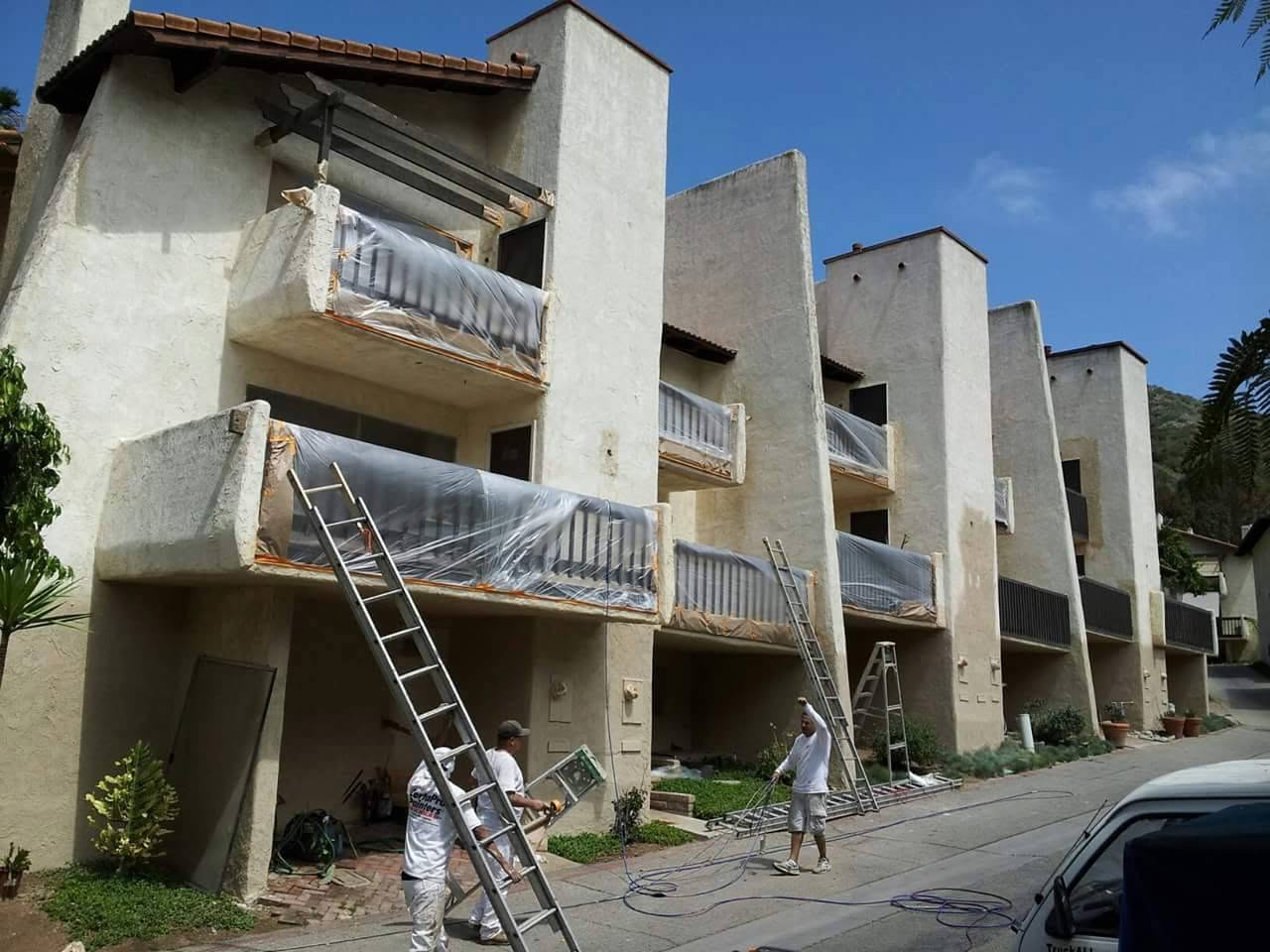 Workers using ladders to install protective plastic sheeting on residential building balconies during renovation