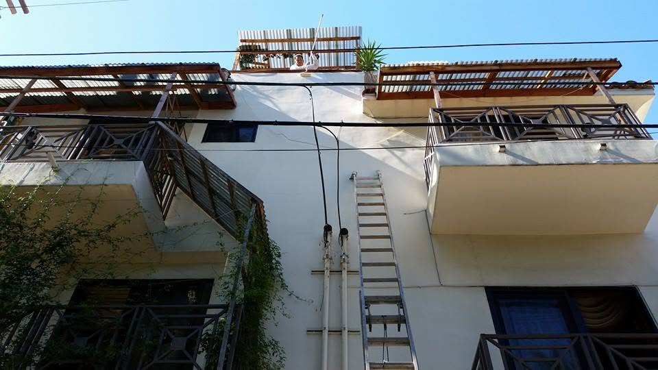 Multi-story residential building facade with wooden roof terraces and metal railings against blue sky