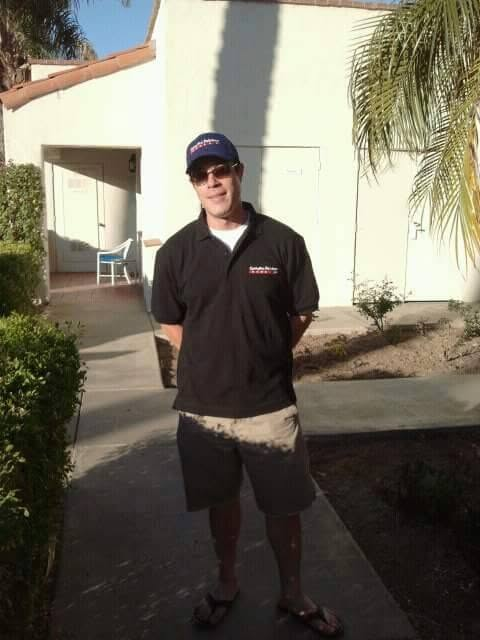 Man in black polo shirt and cap standing in front of white residential building
