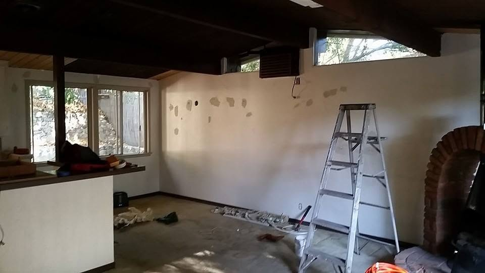 Interior room under renovation with ladder, drywall patches, and large windows overlooking outdoor area