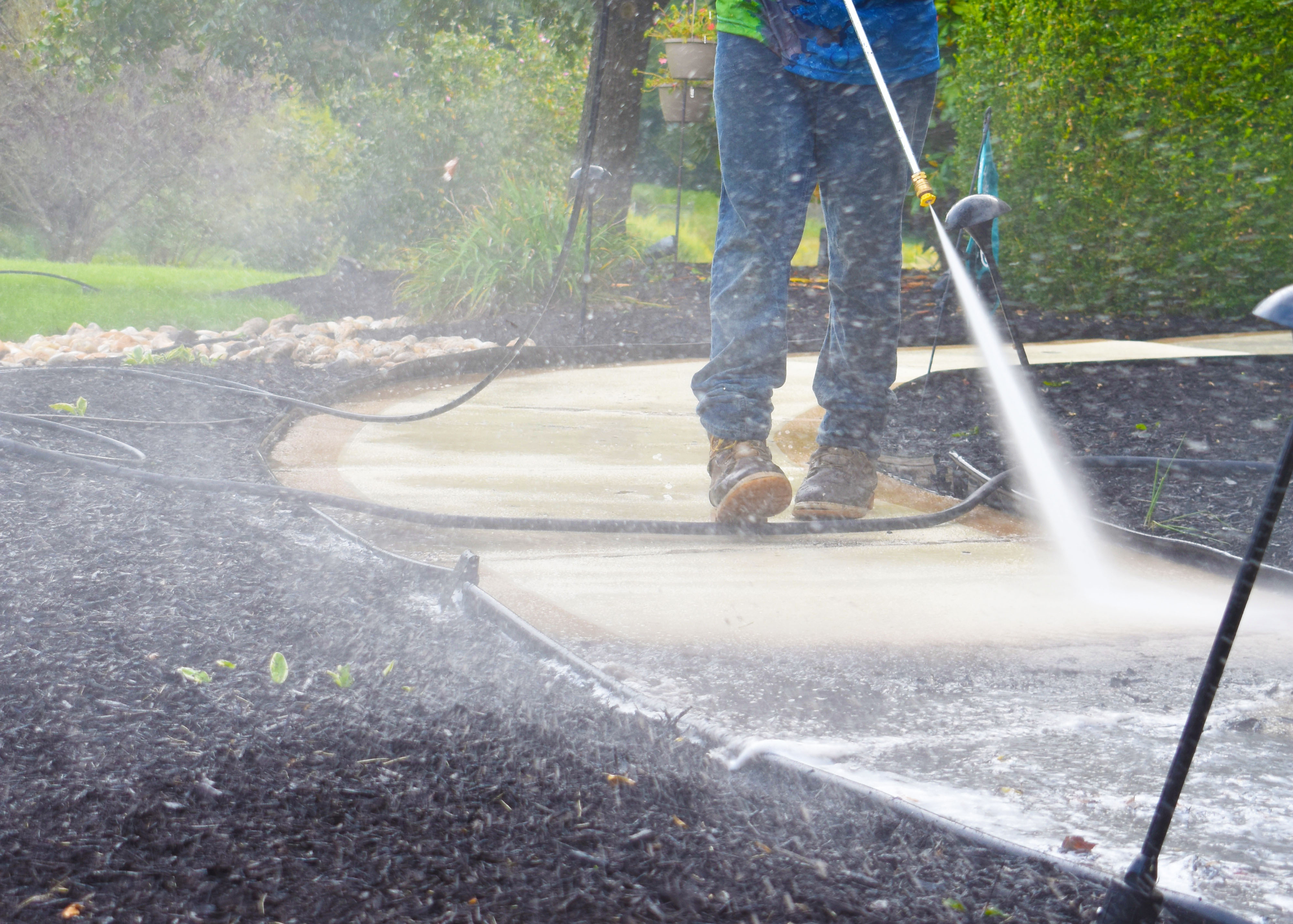 Worker using pressure washer to clean concrete patio in residential garden
