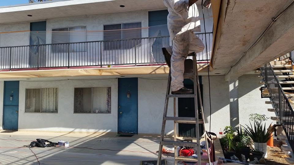 Worker on ladder performing maintenance on multi-story residential building exterior